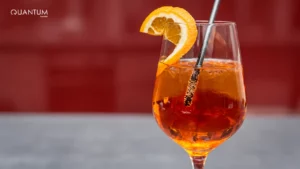 Verre à pied contenant une boisson orangée, des glaçons, une paille et une tranche d’agrume