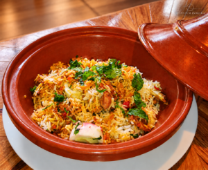 Biryani au poulet Quantum Isoraka, avec des grains de riz longs servi dans un plat en terre cuite sur un fond chaleureux en bois.