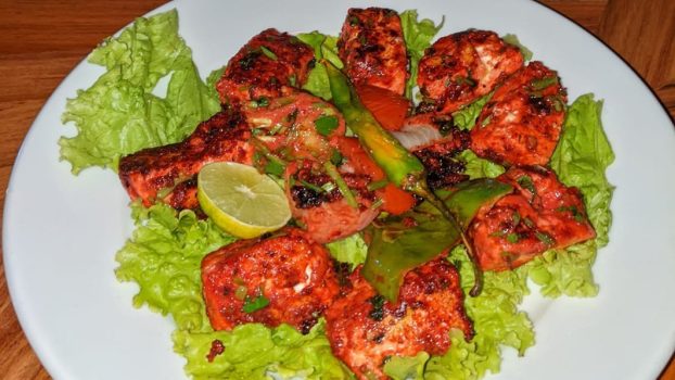 Cubes de paneer marinés et grillés, à la marinade rouge, sur feuilles de laitue avec un demi-citron vert, du piment vert et de l'oignon