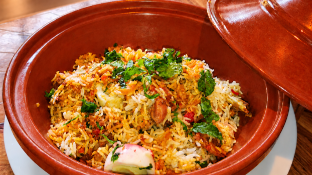 Biryani au poulet Quantum Isoraka, avec des grains de riz longs servi dans un plat en terre cuite sur un fond chaleureux en bois.